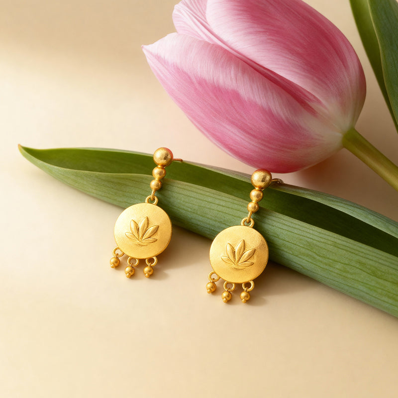 Gold earrings with leaf design on a pink tulip and green leaf background